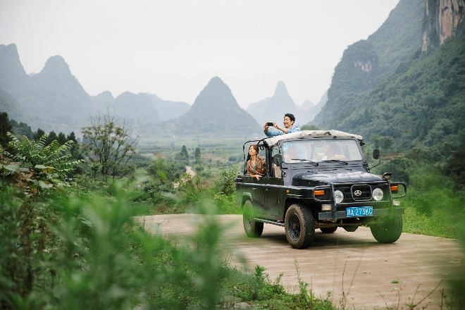 A group of people on a jeep on a dirt road in the mountainsDescription automatically generated with medium confidence